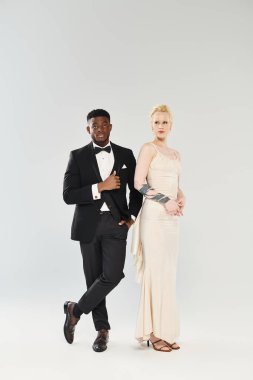 Gelinlik giymiş güzel bir sarışın gelin ve smokinli bir Afrikalı Amerikalı damat stüdyoda yan yana duruyorlar..