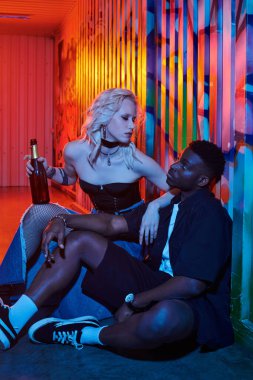 Sarışın bir kadın ve Afro-Amerikalı bir adam duvar yazısıyla kaplı bir sokakta yan yana oturuyorlar..