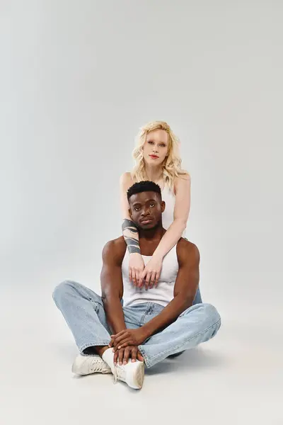 stock image A man sits on the ground supporting a woman on his back, showcasing trust, balance, and connection in a studio setting.