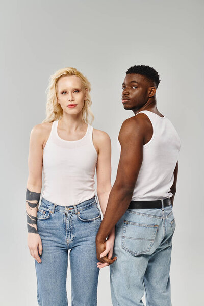 A young multicultural couple standing side by side in a studio against a grey background.