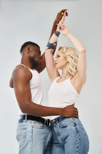 stock image A young interracial couple dancing gracefully together in a studio against a grey background.