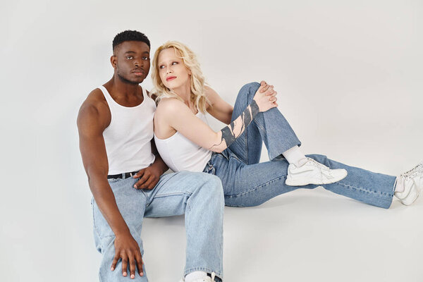 A young man and woman of different races strike a pose together in a studio against a grey backdrop.