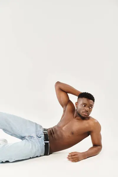 stock image A young African American man lies sprawled shirtless on the ground, exuding sensuality and tranquility in a studio setting.