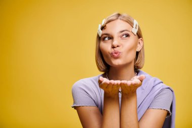 Sarı arkaplanda poz veren kısa saçlı, güzel giyimli, pozitif kadın.