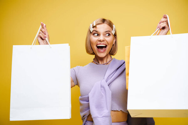 joyous good looking woman with short hair posing on yellow background with shopping bags in hands