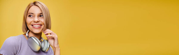 trendy joyous woman with short blonde hair and headphones enjoying music on yellow backdrop, banner
