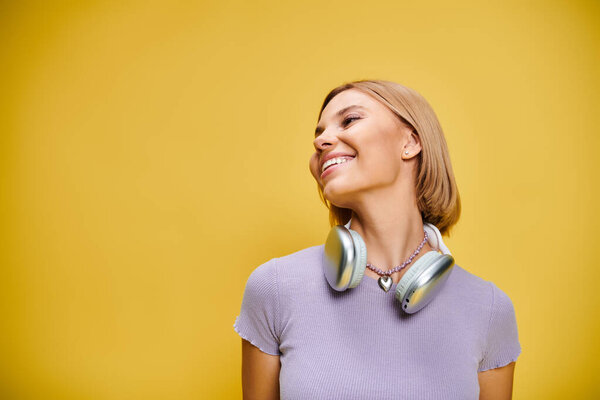 exquisite joyous woman with short blonde hair and headphones enjoying music on yellow backdrop