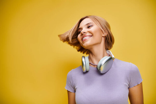 polished joyous woman with short blonde hair and headphones enjoying music on yellow backdrop