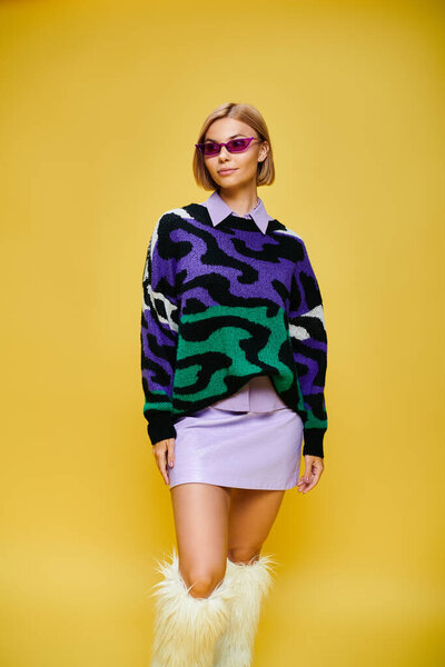 beautiful cheerful woman with short hair and sunglasses in vibrant attire posing on yellow backdrop