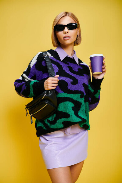 appealing cheerful woman with stylish sunglasses in vibrant attire posing with coffee cup in hand