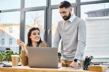 Bir erkek ve kadın, modern ofis ortamında yoğun bir şekilde dizüstü bilgisayara odaklanmış bir beyin fırtınası yapıyorlar..