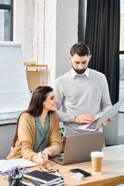 Bir erkek ve bir kadın ortak çalışma oturumunda, dizüstü bilgisayarla bir masada oturup, şirket ofis ortamında bir projeyi tartışıyorlar..