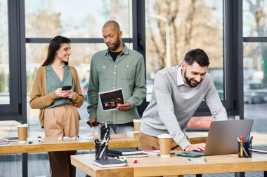 İki erkek ve bir kadın bir projede işbirliği yapıyorlar. Modern bir ofis ortamında dizüstü bilgisayarla çok meşguller..