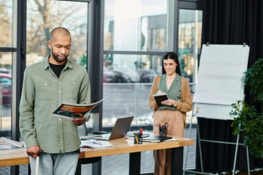 Bir erkek ve bir kadın, profesyonel bir ofis ortamında bir masanın önünde fikir alışverişinde bulunuyorlar..