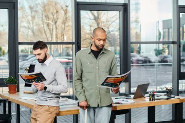 Profesyonel giysiler giymiş iki işadamı bir ofis ortamında yan yana duruyorlar..
