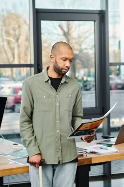 Engelli bir adam masanın önünde duruyor, bir şirket ofisinde çizelgeleri tutuyor..