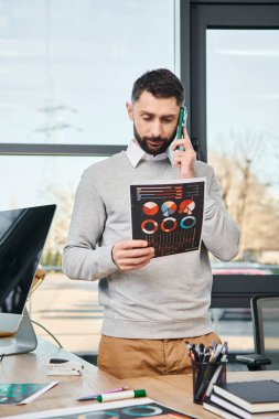 Şirket ofisinde çalışan bir adam cep telefonuyla konuşurken çizelgeleri tutuyor..