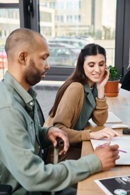 Engelli bir erkek ve bir kadın, kurumsal bir ortamda bir masada oturuyorlar..