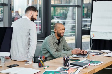Masasında özenle bir proje üzerinde çalışan bir adam, önünde duran dizüstü bilgisayara odaklanmış, bir ofis ortamının ortasında, çeşitlilik ve kapsama