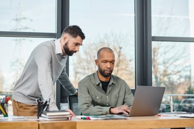 Profesyonel ofis ortamında bir dizüstü bilgisayarda işbirliği yapan iki adam, odaklanmış ve üretken, çeşitlilik ve kapsama