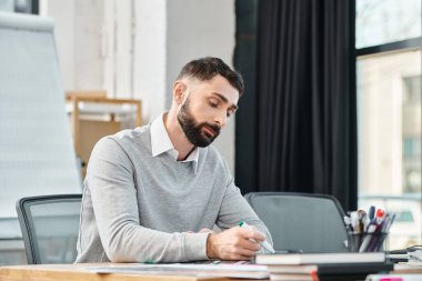 Çalışmaya dalmış bir adam yoğun bir ofisin şık bir masasında, kurumsal bir atmosferle çevrili..