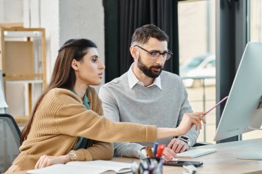 Bir erkek ve bir kadın birlikte oturuyorlar, bilgisayar ekranına odaklanmış, modern ofis ortamında bir iş projesi üzerinde çalışıyorlar..