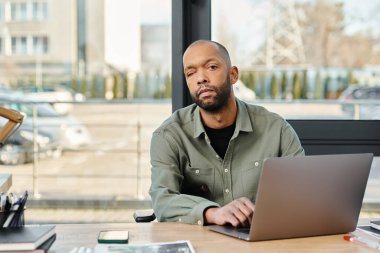 Engelli adam işe daldı, yoğun bir ofis ortamında dizüstü bilgisayarın önünde oturuyor..