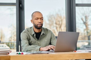 Masasında oturmuş, dizüstü bilgisayarına odaklanmış, modern ofis ortamında bir proje üzerinde çalışan Myasthenia Gravis 'li bir adam..