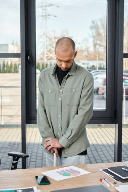 A man with myasthenia gravis stands confidently in front of a wooden table in a bustling office, immersed in a collaborative project. clipart