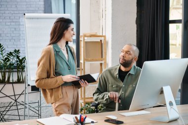 A disabled man with myasthenia gravis and a woman are brainstorming in front of a computer in a modern office setting. clipart