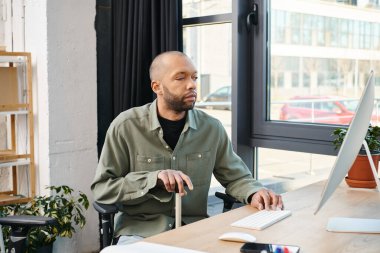 Myasthenia Gravis 'i olan engelli bir Afrikalı Amerikalı bilgisayar ekranına odaklanmış, klavyeye yazı yazıyor, şirket ofisinde dijital bir proje yaratıyor..