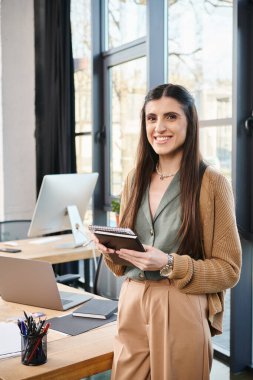 Masada duran bir iş kadını, elinde parlak bir ofis ortamında bir tablet tutuyor, kurumsal kültüre dalmış..