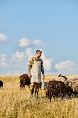 Koyun ve kuzularla çevrili sakallı, kovalı, çalışkan, çekici bir çiftçi.
