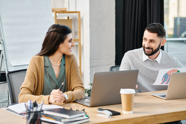 A man and woman passionately engrossed in their laptops at a table, actively working on a project in a corporate environment.