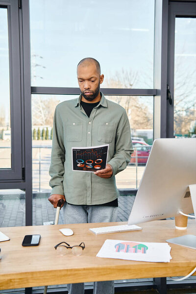 A man stands confidently in front of a desk, holding a book as he prepares for a productive day of work in an office setting.