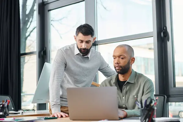 stock image Two men in a corporate office are focused on a laptop screen, actively engaged in a discussion or project analysis, diversity and inclusion