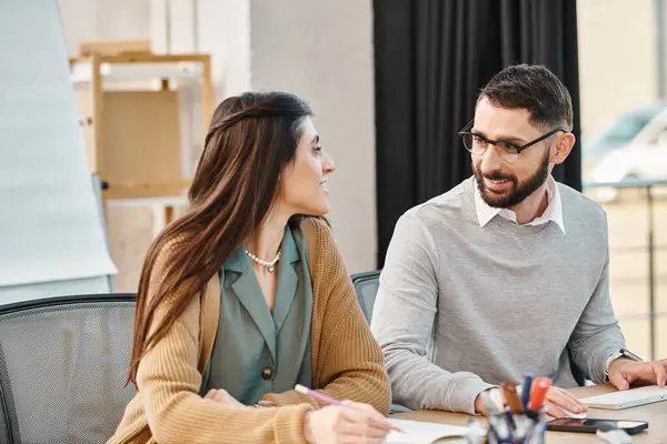 stock image A man and a woman sit at a table, discussing a project in a business setting.