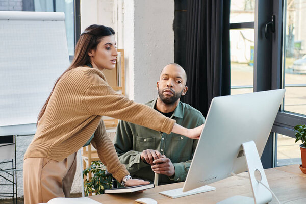 Мужчина с миастенией и женщина, занимающиеся совместной работой, сидящие за столом в офисе, сосредоточенные на компьютерном экране.