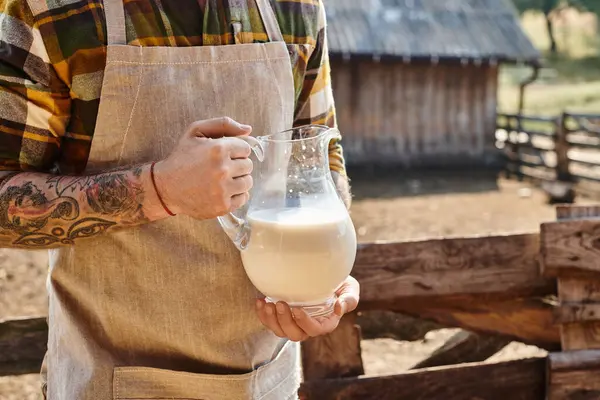 彼の農場で新鮮なミルクの大きな瓶を持っているタトゥーとハードワーキング男性の見た目 — ストック写真