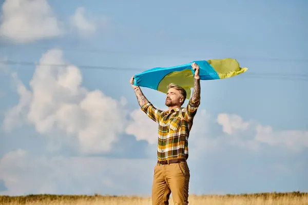 stock image appealing Ukrainian man in casual attire posing with national flag, scenic landscape, modern farmer