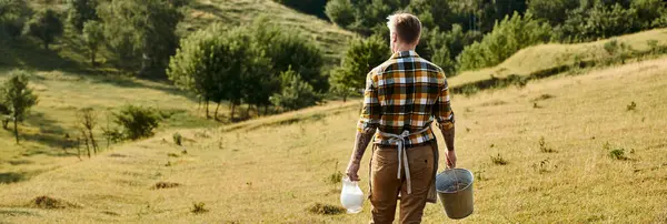 手のバケツとミルクの瓶で歩くハードワーキング現代農民のバックビュー バナー — ストック写真