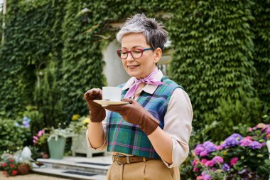 attractive joyful mature woman drinking hot tea at breakfast in garden of her house in England clipart