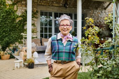 sofistike, olgun, neşeli, kısa saçlı kadın İngiltere 'deki evinin yakınındaki kameraya gülümsüyor.