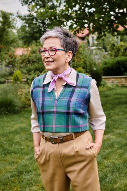 Sofistike giyinmiş zarif olgun bir kadın İngiltere 'deki evinin yakınında poz veriyor ve başka tarafa bakıyor.