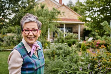 sophisticated mature joyful woman with short hair smiling at camera near her house in England clipart