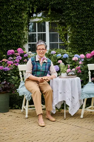 stock image cheerful mature woman sitting in garden at tea time near house in England and looking at camera
