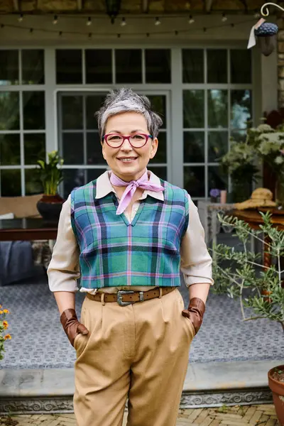 Aristokratik neşeli olgun kadın İngiltere 'deki evinin yanında poz veriyor ve kameraya bakıyor.