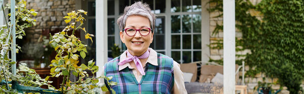 сложная зрелая веселая женщина с короткими волосами, улыбающаяся перед камерой возле своего дома в Англии, баннер