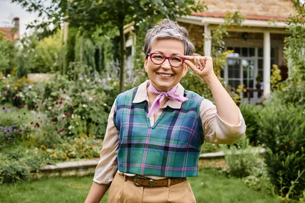 sofistike, olgun, neşeli, kısa saçlı kadın İngiltere 'deki evinin yakınındaki kameraya gülümsüyor.