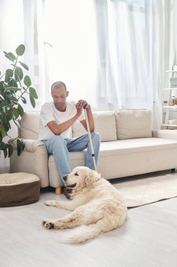 Engelli bir Afrikalı Amerikalı adam, miastenya gravis 'i olan sadık Labrador köpeği ile kanepede dinleniyor, çeşitlilik ve kapsamı destekliyor..